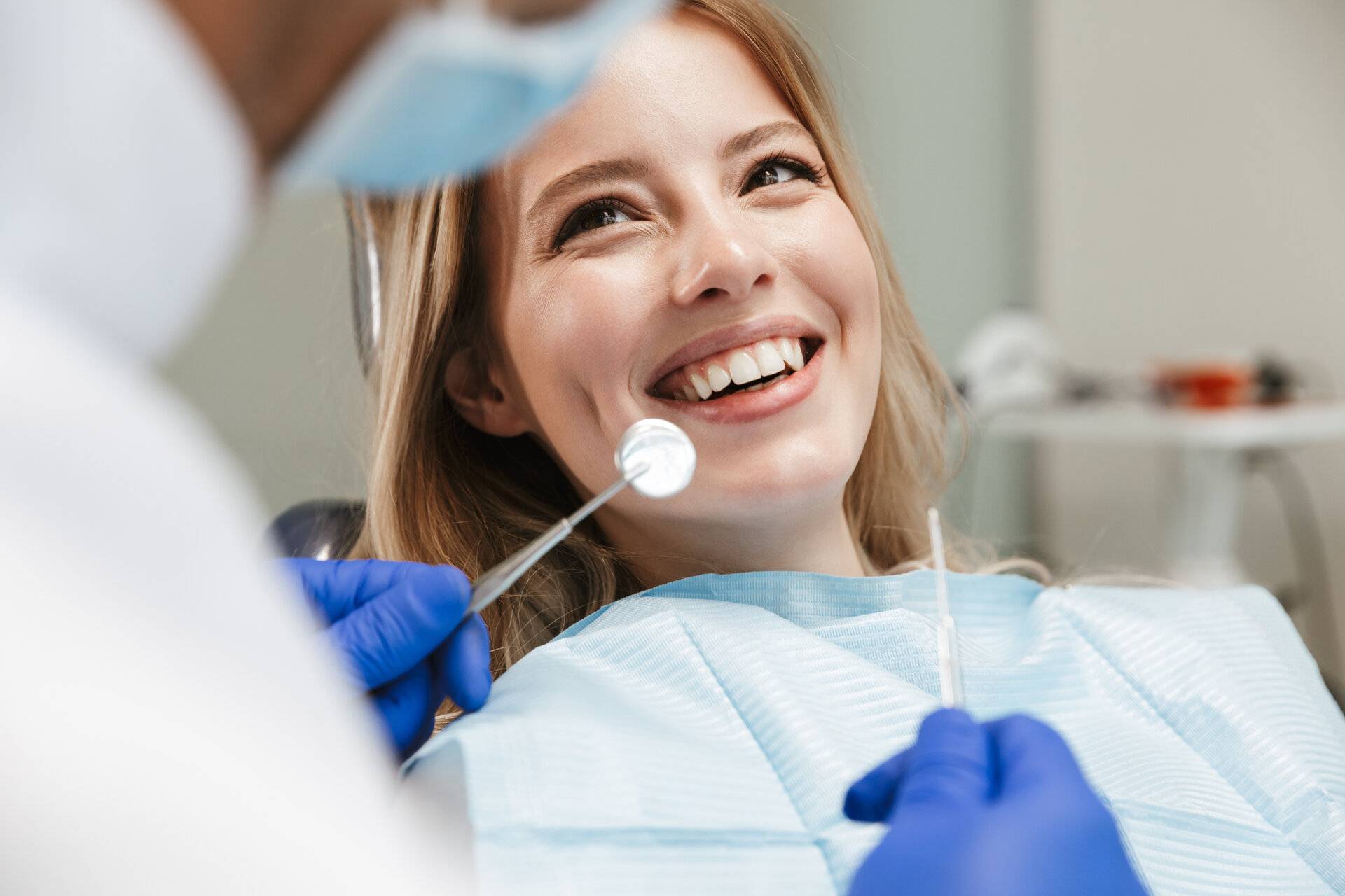 Bild einer hübschen jungen Frau, die im Behandlungsstuhl sitzt, während ein professioneller Zahnarzt ihre Zähne kontrolliert.