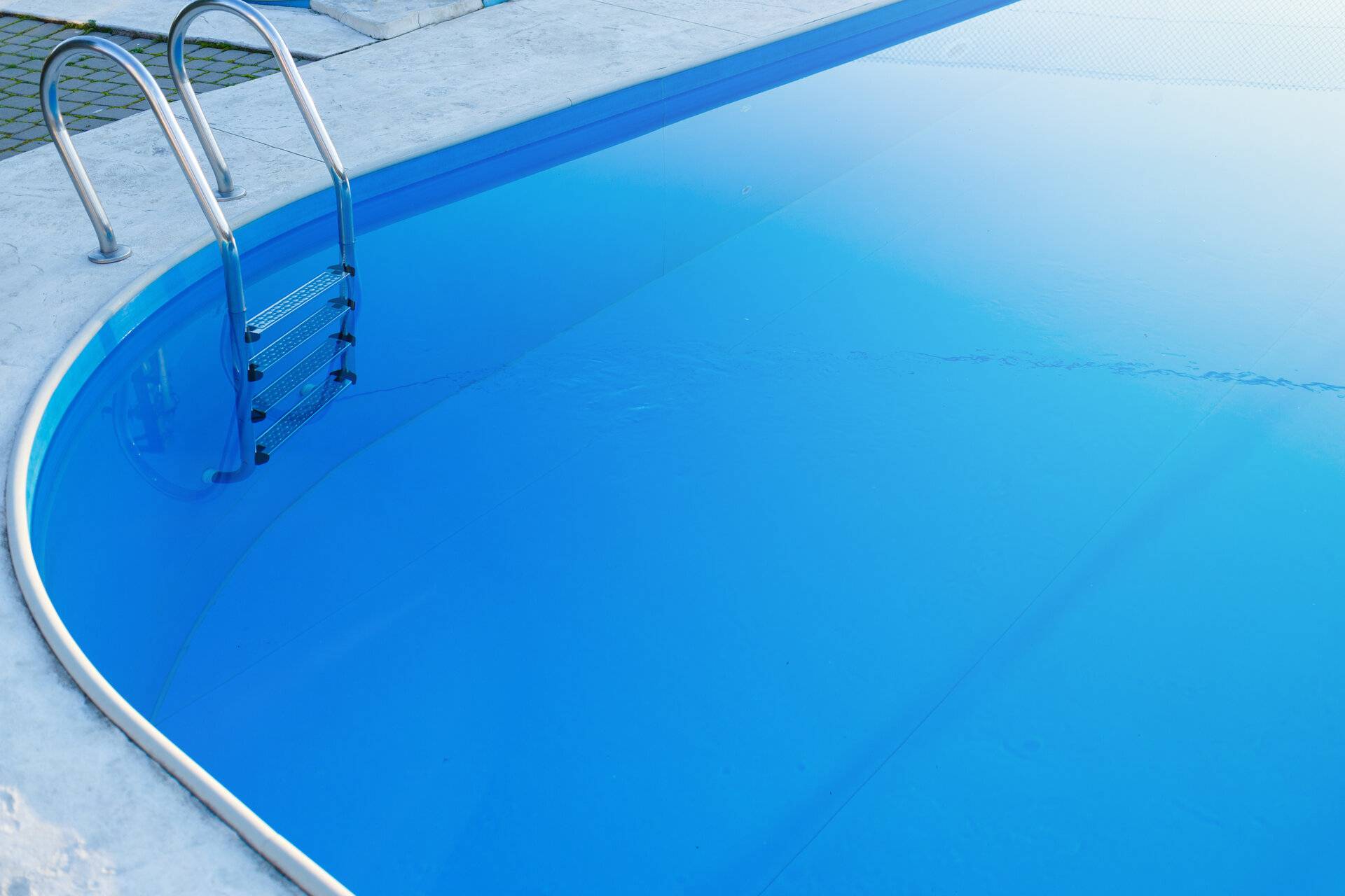 Nahaufnahme eines Teils eines GFK Swimmingpools mit einer Leiter aus Edelstahl und blauem Wasser bei Sonnenuntergang