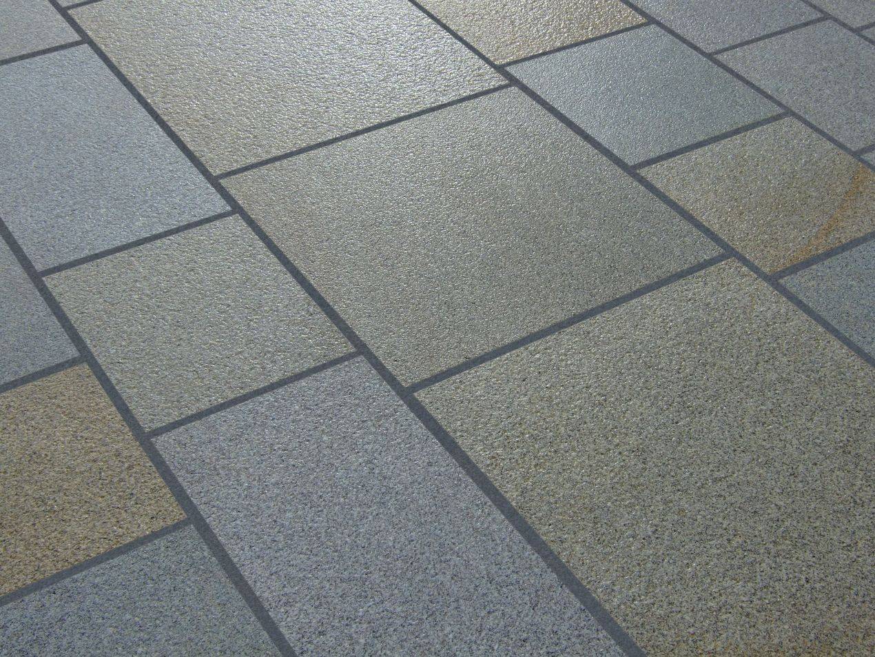Natursteinplatten in unterschiedlichen Beige- und Grautönen, rechteckig verlegt auf einer Außenfläche mit klarer Fugenstruktur