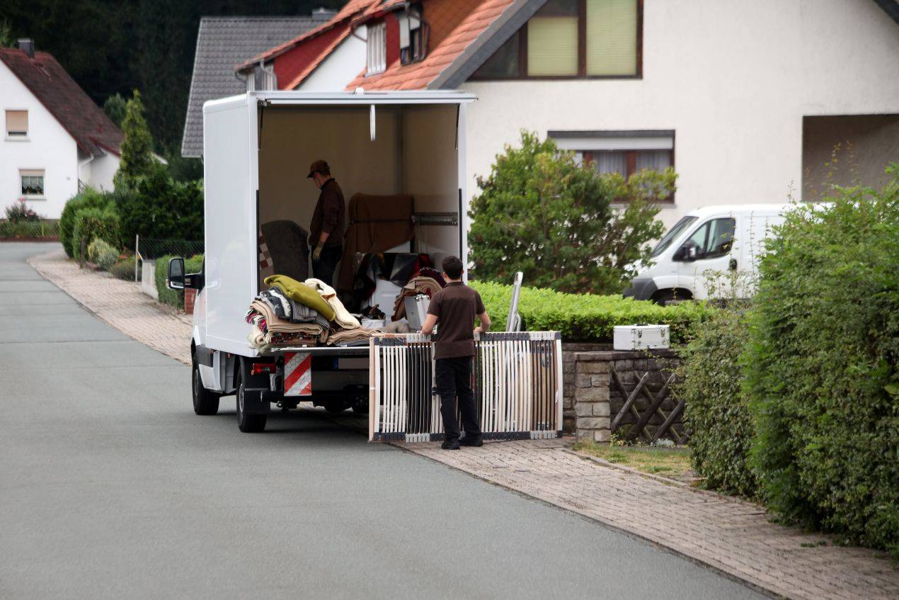 Zwei Personen verladen Moebel bei einer professionellen Entrümpelung Beckum in einen Transporter vor einem Wohnhaus