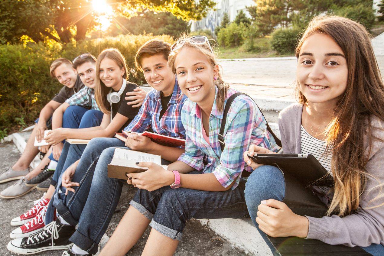 Gruppe von Schuelerinnen und Schuelern sitzt draussen mit Notizbuechern und Tablets – entspannte Lernatmosphaere auf Klassenfahrt Muenchen