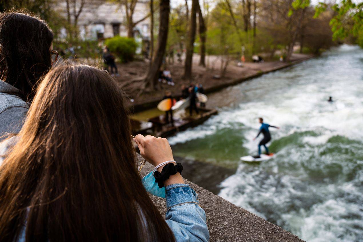 Zwei Maedchen beobachten Surfer am Eisbach im Englischen Garten – ein Highlight jeder Klassenfahrt Muenchen