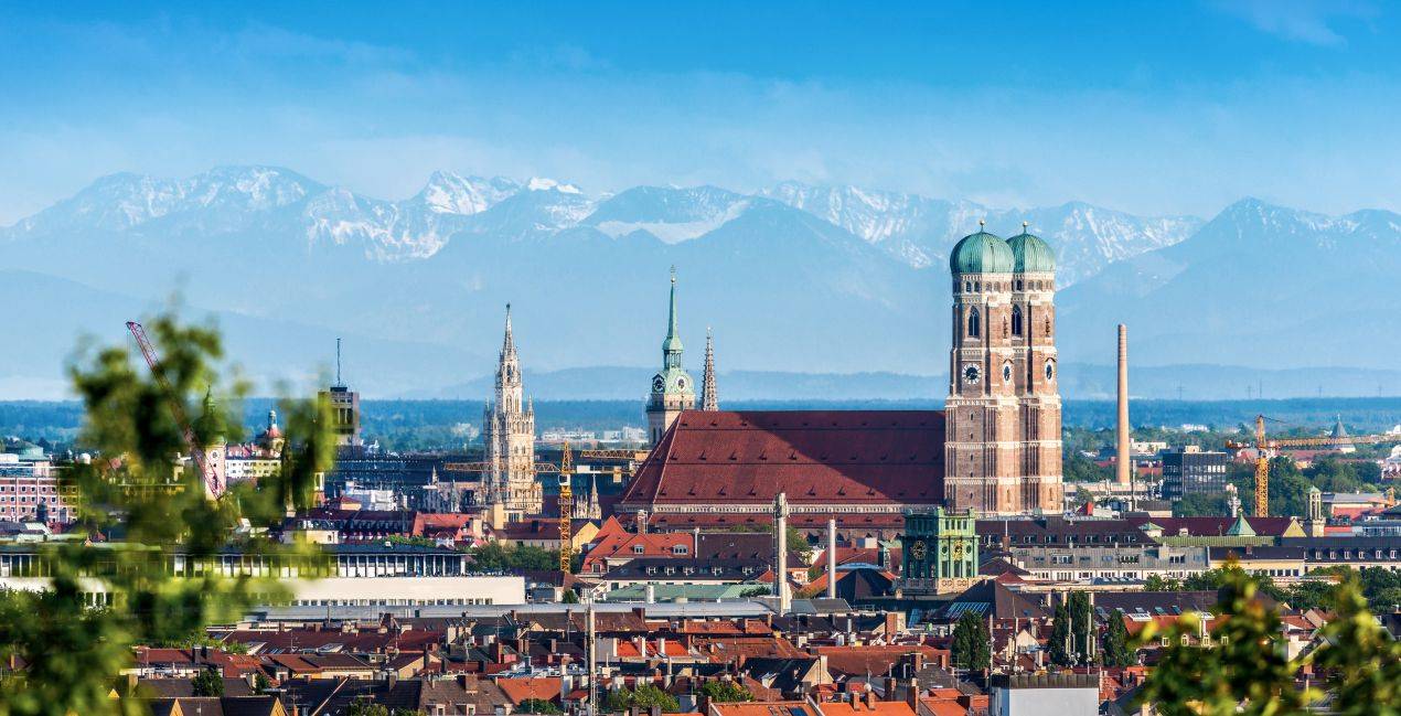 Blick auf die Frauenkirche und Innenstadt von Muenchen mit Alpen im Hintergrund – idealer Eindruck einer Klassenfahrt Muenchen